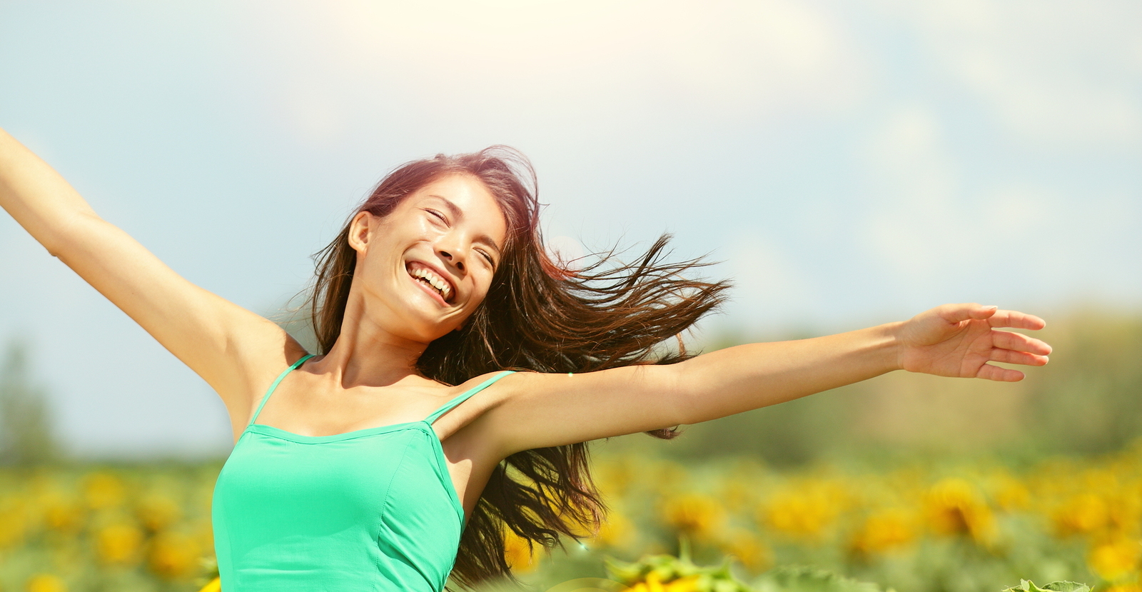 Happy woman in sunflower field. Summer girl in flower field cheerful and joyful. Multiracial Asian Caucasian young woman dancing, smiling elated and serene with arms raised up.
