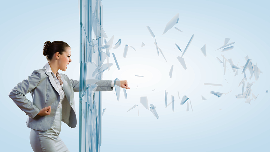 Young determined businesswoman breaking glass with karate punch